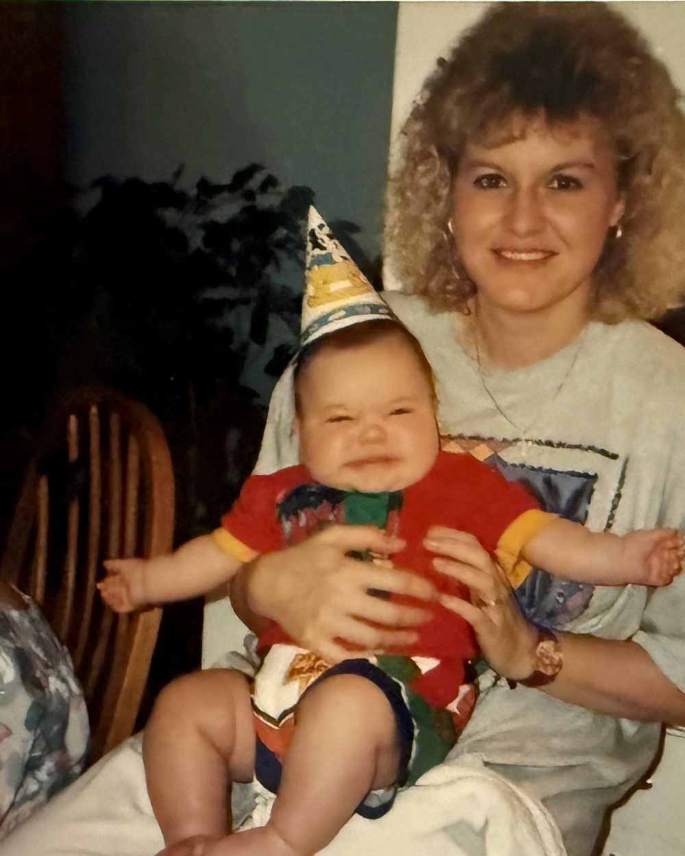 A woman holding a smiling baby in a party hat, from a digitized print